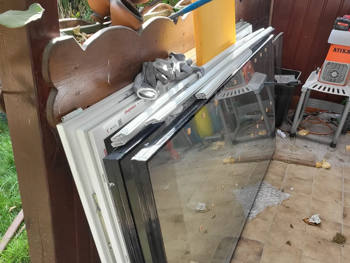 Neue weiße Fenster mit Aluplast-Profil und Schutzfolie, an eine Holzwand gelehnt