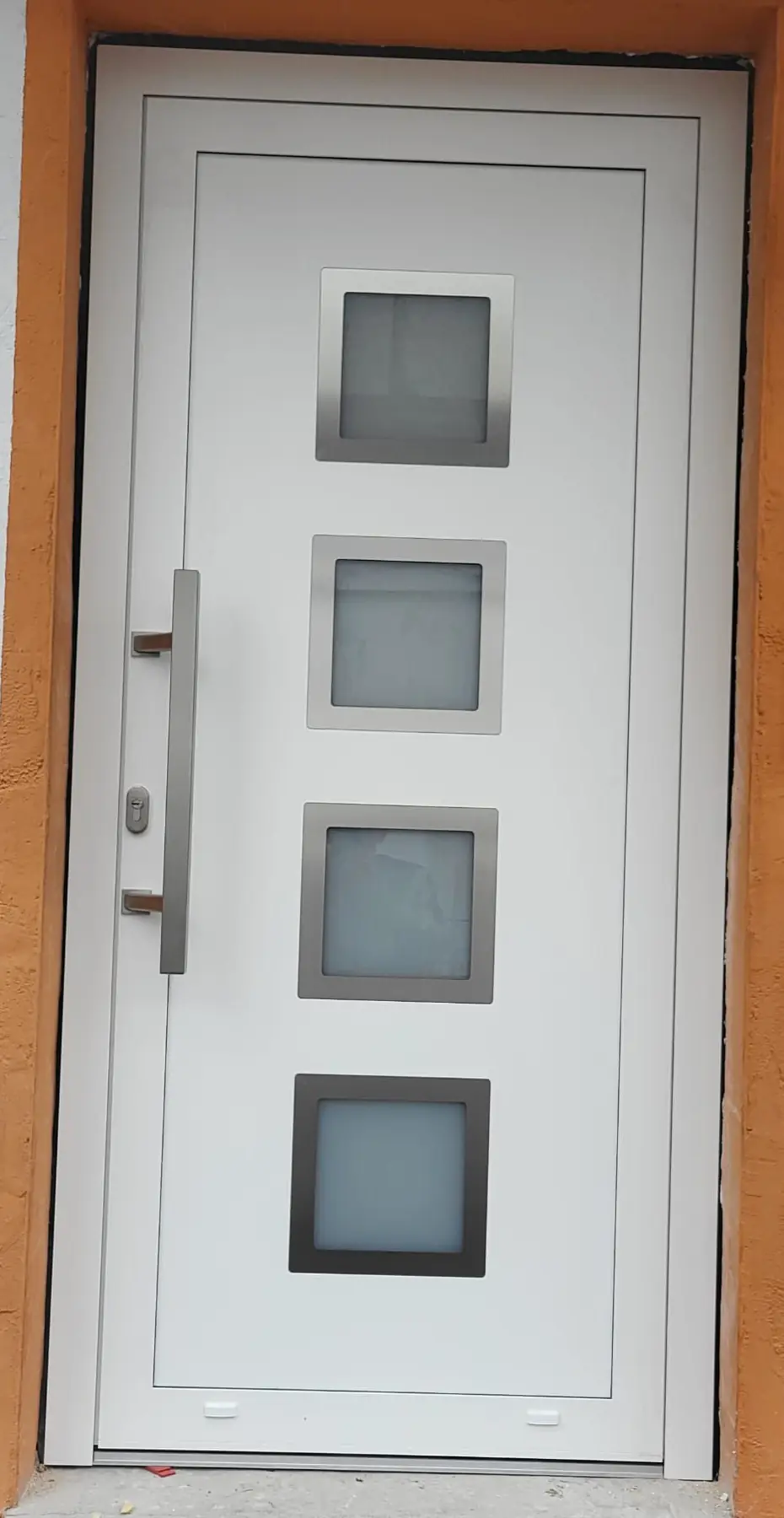 Neu eingebaute weiße Haustür mit vier quadratischen Glasfeldern und langem Edelstahlgriff