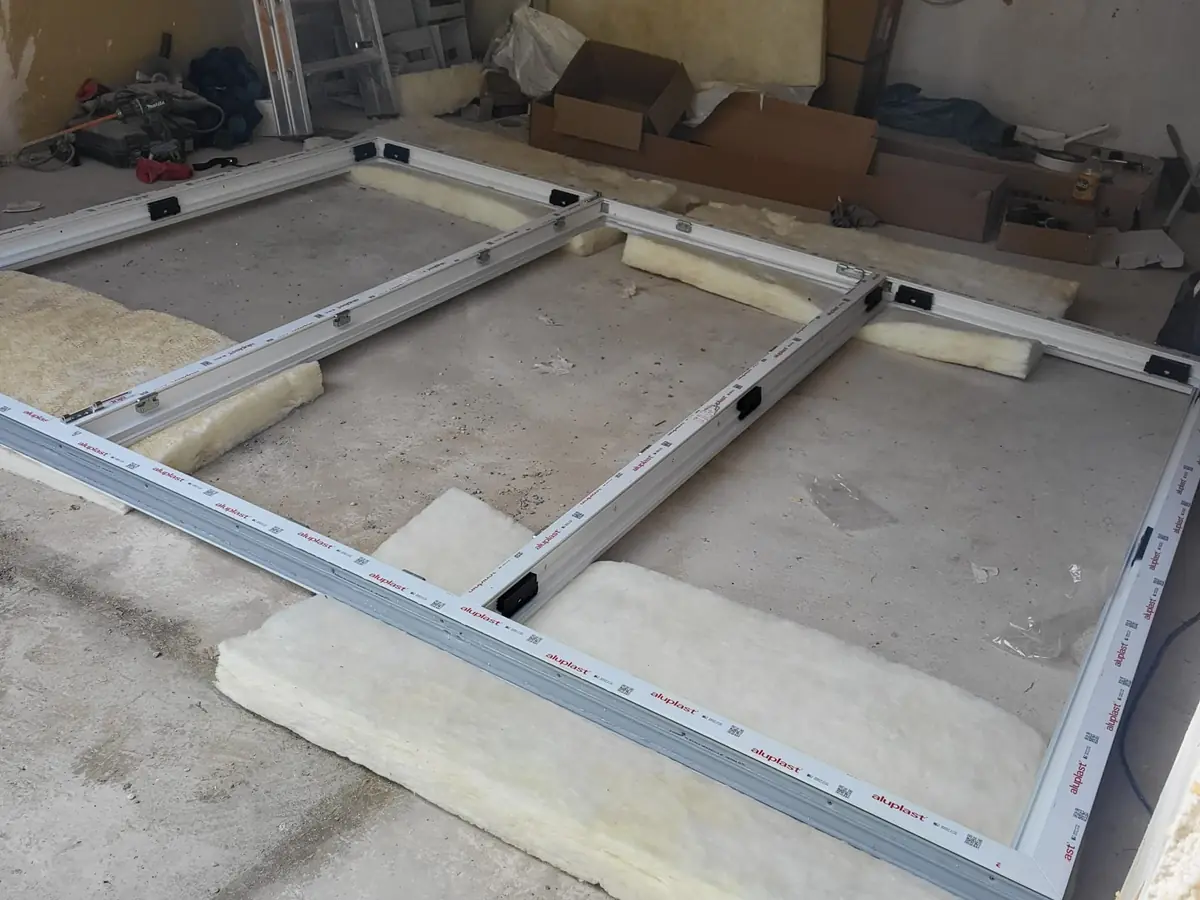 Weiße Fensterrahmen mit Aluplast-Schutzfolie liegen auf dem Boden einer Baustelle