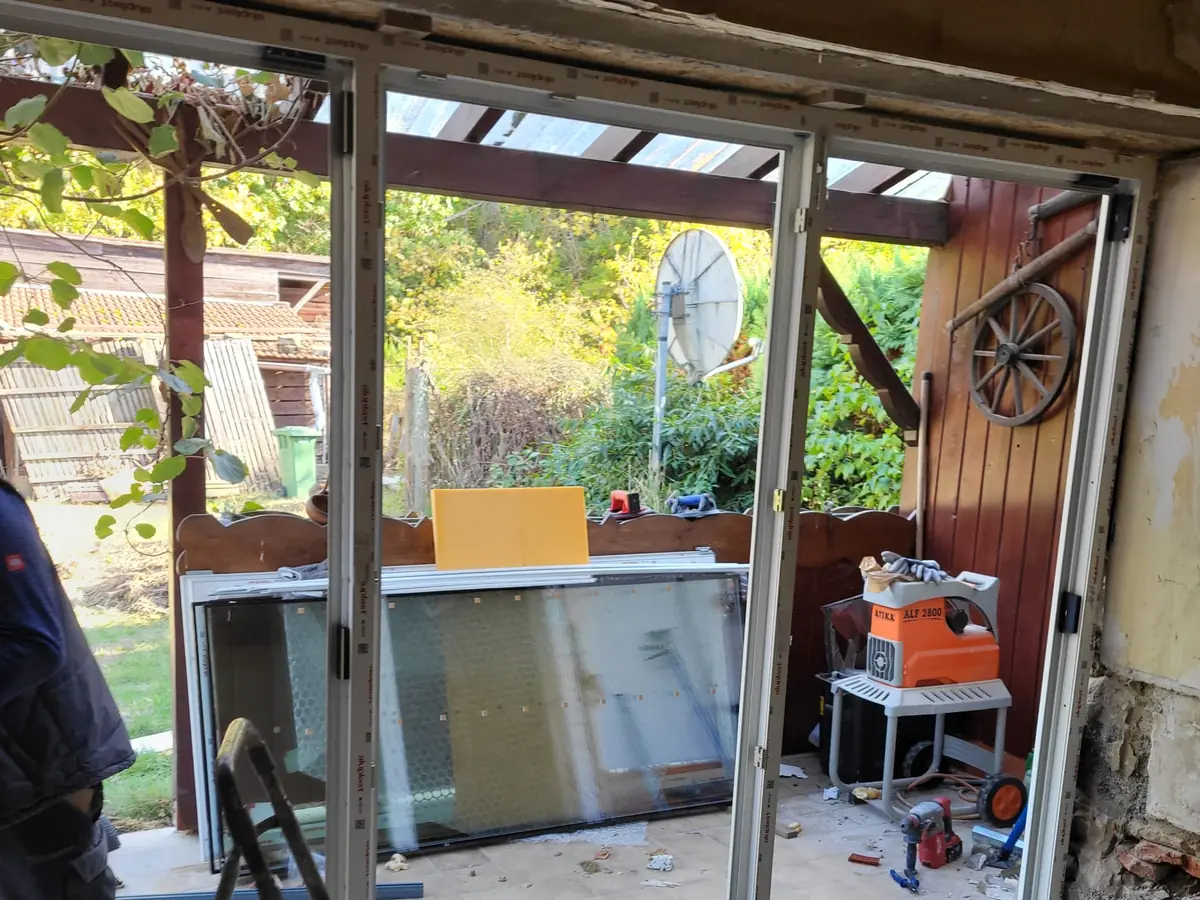 Große Terrassentür-Elemente mit weißen Rahmen beim Einbau in eine Maueröffnung, davor eine Trittleiter